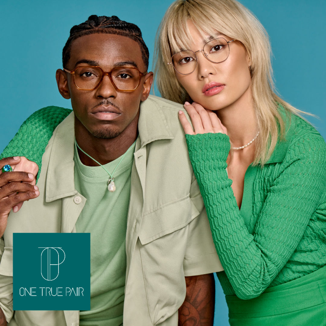 A black man wearing a green shirt under a light green button up models thick gold modified aviator frames, posing next to an asian woman with blond hair and a light green sweater modeling delicate gold rounded frames. One True Pair logo located on bottom left. 