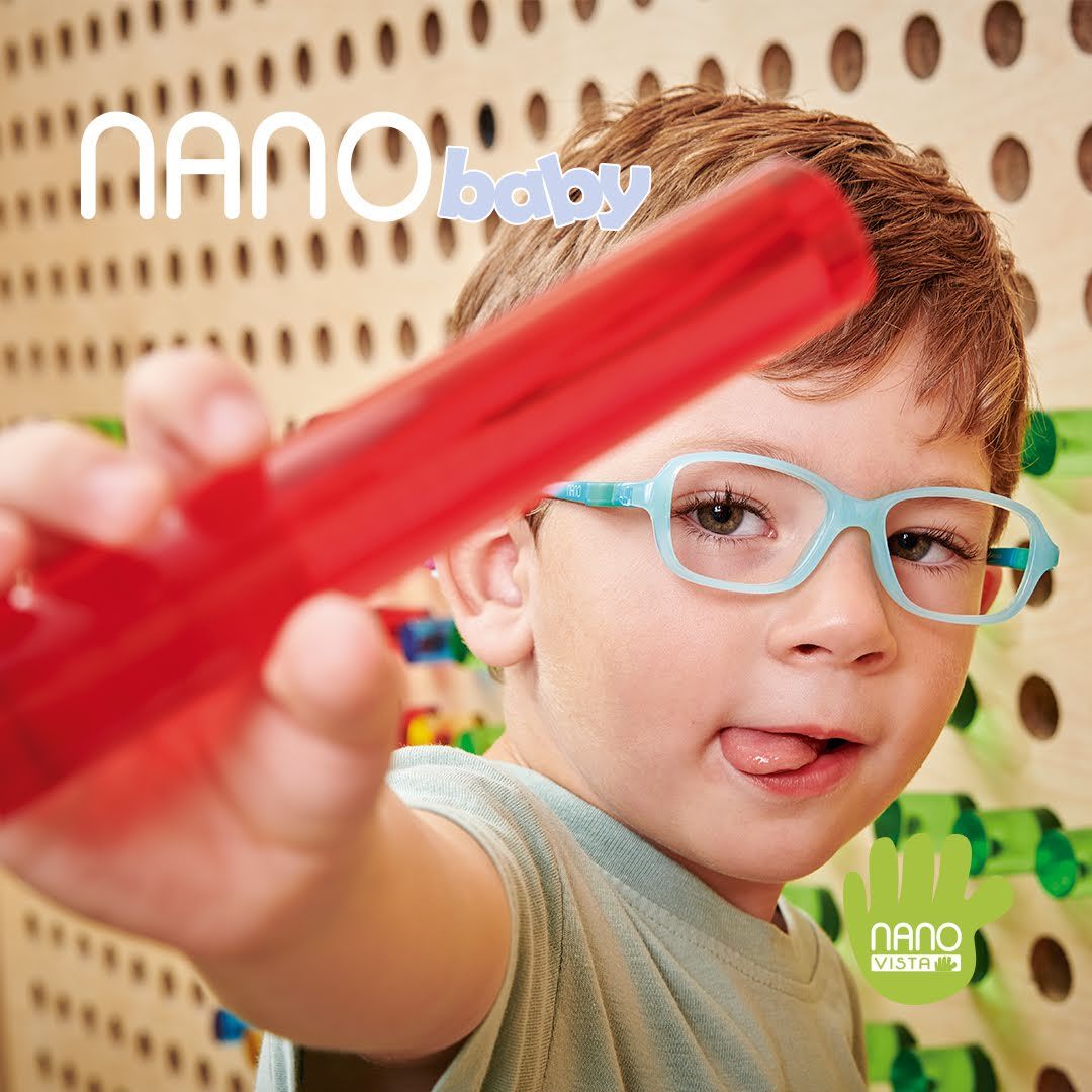 Child with a grey shirt standing against a colorful pegboard, wearing light blue frames and showing off a red glasses case. Nano Baby logo located in the upper left, Nano Vista logo located on bottom right.