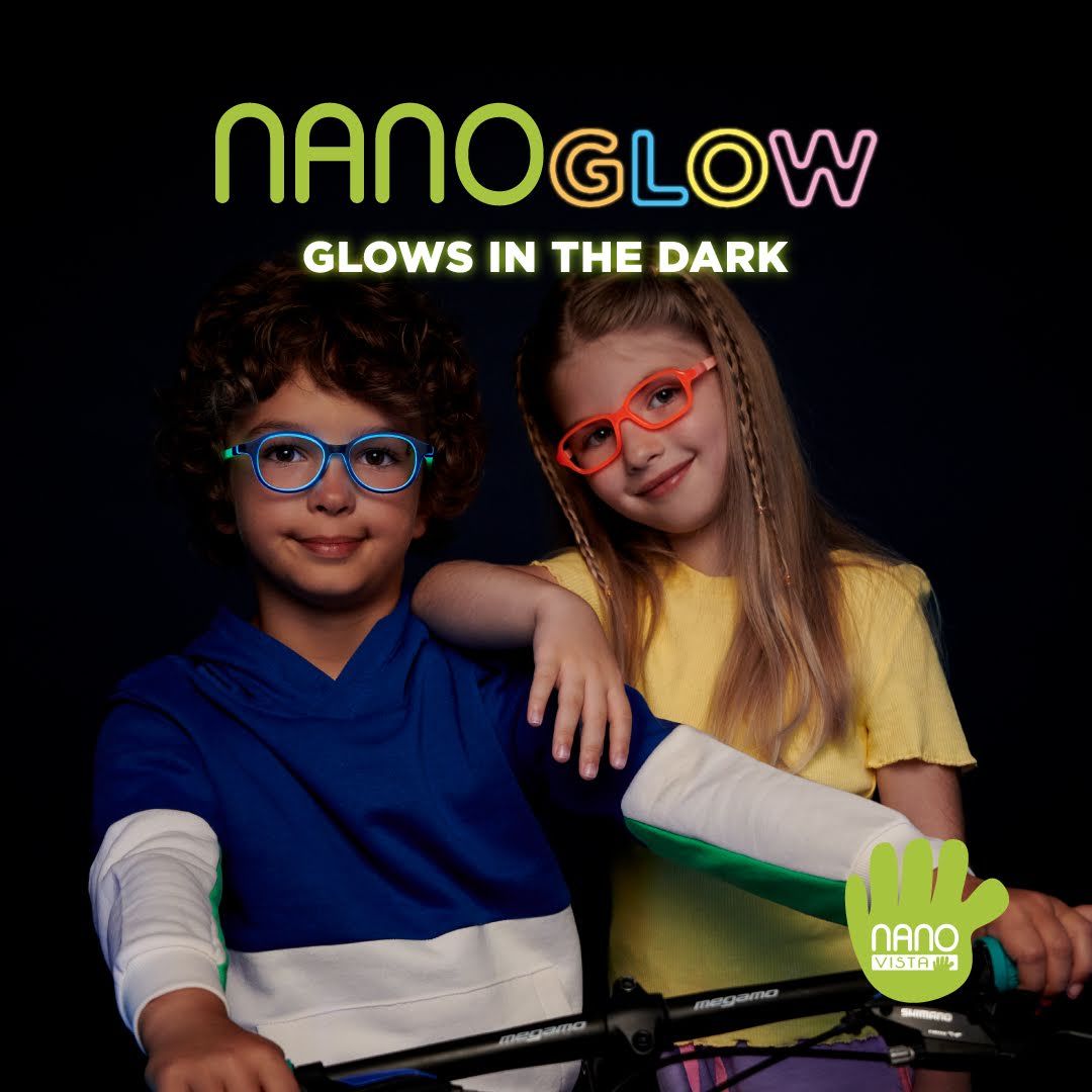 A boy with curly dark hair wearing a blue hoodie with white and green sleeves and blue glowing frames sits on a bicycle while a girl in a yellow shirt with long brown hair and red glowing frames, stands next to him with her arm on his shoulder. Nano Glow Glows in the dark is written across the top of the image, Nano Vista logo located on bottom right.