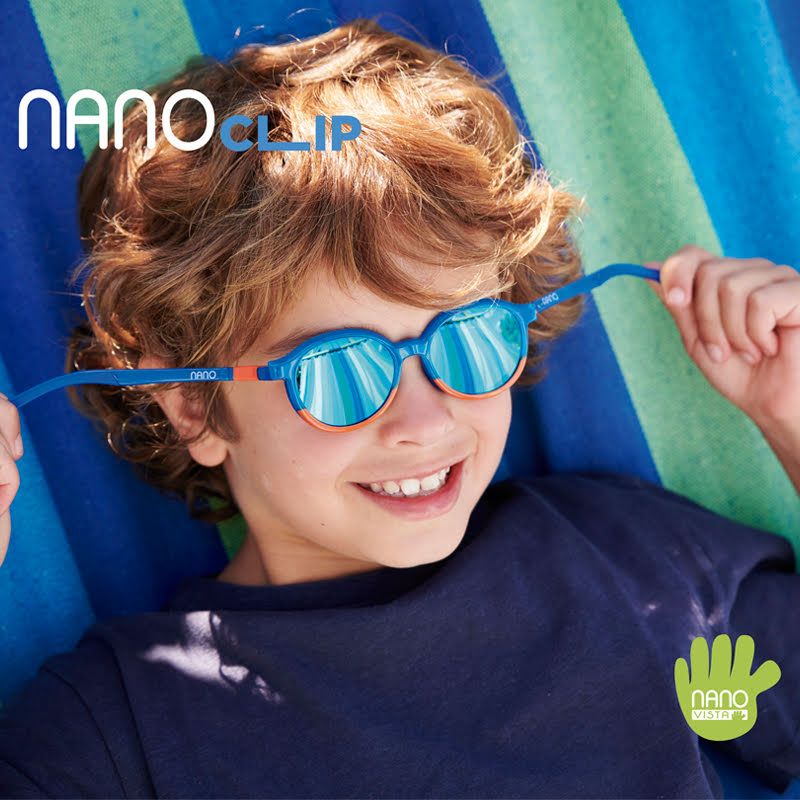 Boy with curly  hair and dark blue shirt lounging in a striped hammock and pulling the temples of his glasses sideways away from his face. Nano Clip logo located in the upper left, Nano Vista logo located on bottom right.