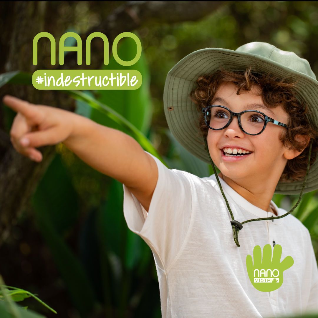 A young boy with brown curly hair wearing a green bucket hat and white t-shirt and mottled round frames, stands in front of trees pointing excitedly off screen left. Nano #indestructible logo in upper left corner, Nano Vista logo in bottom right corner. 