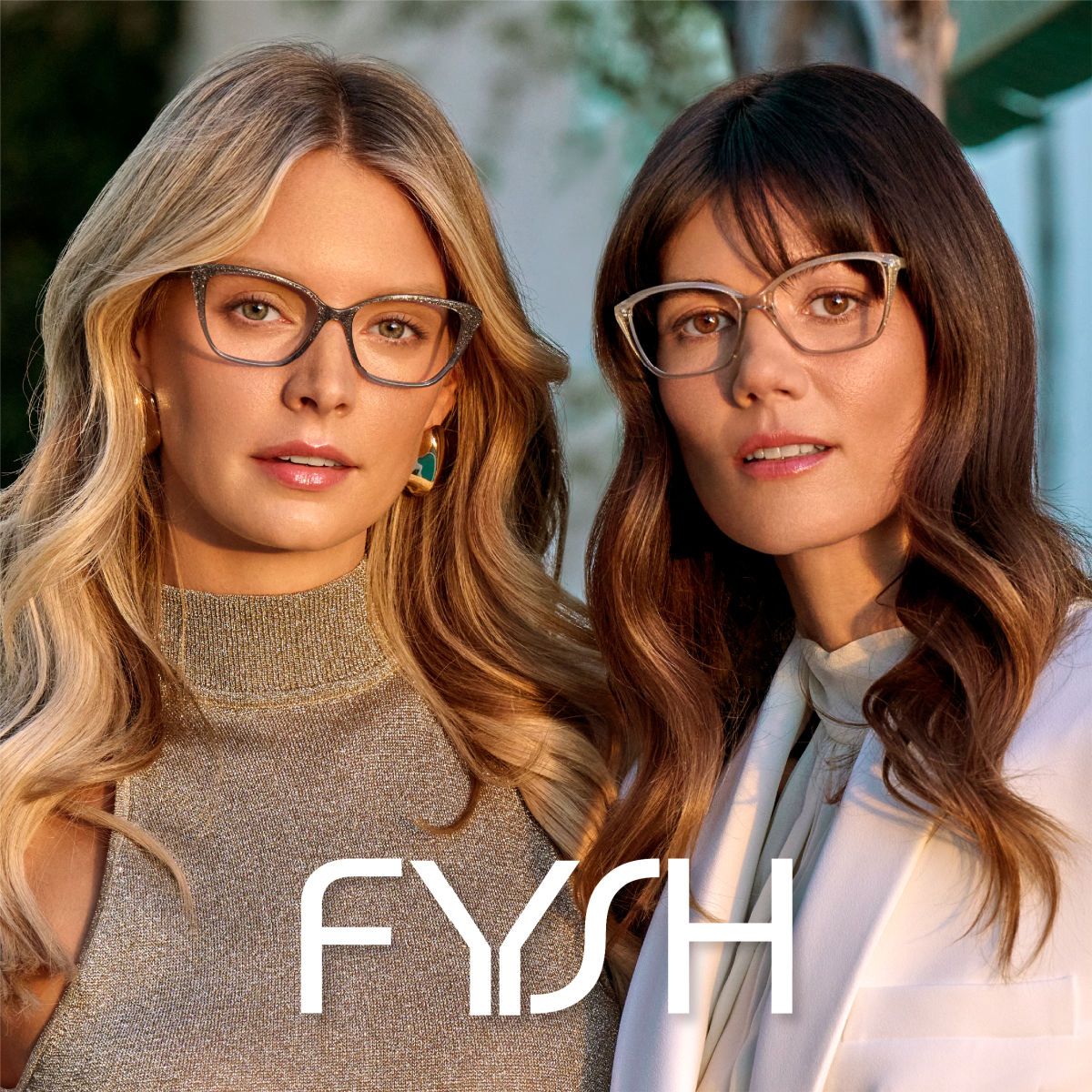 Two female models with long wavy hair facing the camera showcasing stylish frames similar to cat eye frames. The Fysh logo is displayed in white across the bottom center of the image.