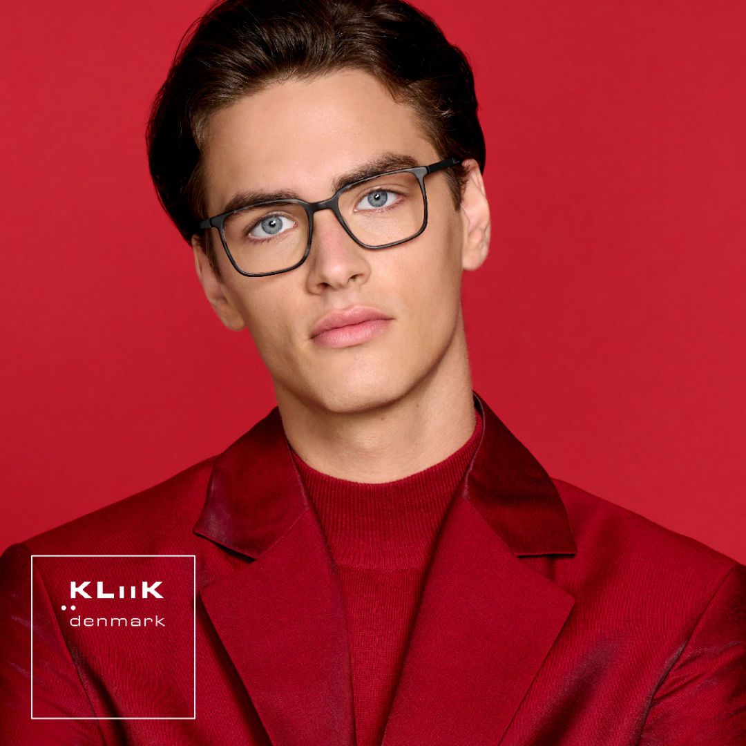 Man with short brown hair wearing a shiny red shirt against a red background, models bold square black frames. KLiiK denmark logo in a white box on the bottom left of the image.