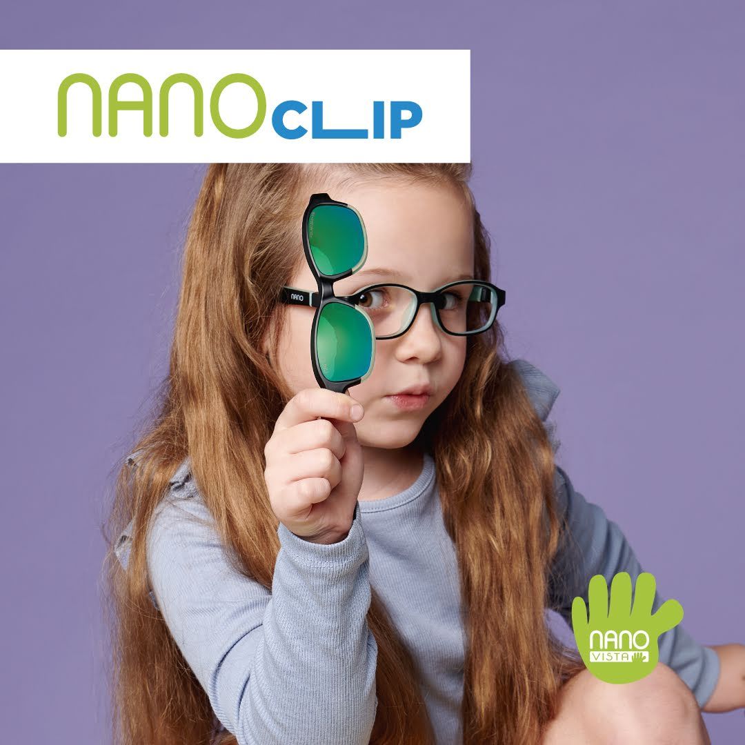 Young girl with red hair half up, wearing a light purple shirt and crouching against a darker purple background, wearing dark oval frames and holding up clip on sunglasses frames. Nano Clip logo located in the upper left, Nano Vista logo located on bottom right.