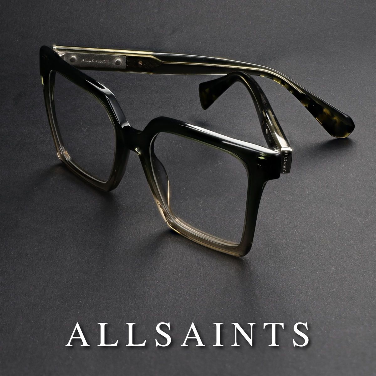 Thick square frames propped open with temples crossed, facing lower right, on a grey background. AllSaints logo in white text along the bottom of the image.