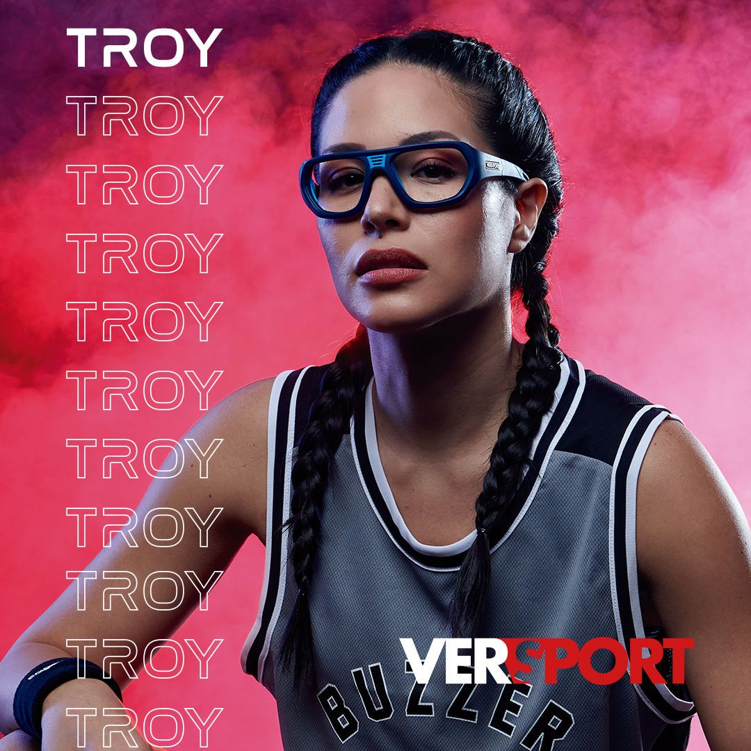 A woman with two long braids wears a grey and black basketball jersey modeling dark blue Versport frames. TROY is written multiple times down the left side of the image and the VERSPORT logo is on the bottom right.
