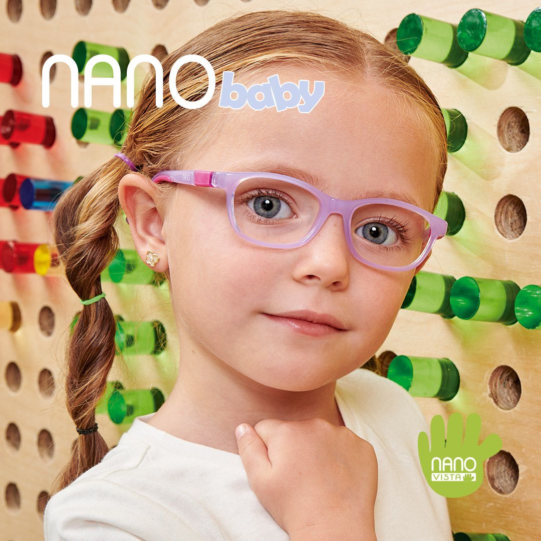 Child with long twisted blond hair stands against a colorful peg board wearing pale pink frames with dark pink accents on the temple. Nano Baby logo located in the upper left, Nano Vista logo located on bottom right.