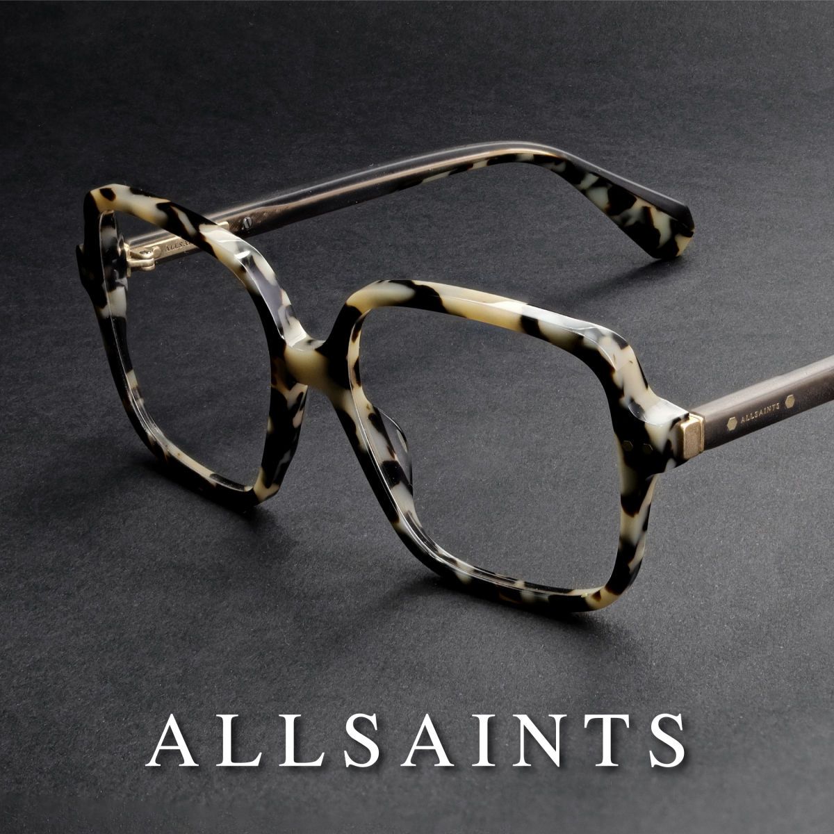 Black and white mottled frames sitting propped open, facing lower left, on a grey surface. White AllSaints logo runs along the bottom of the image.